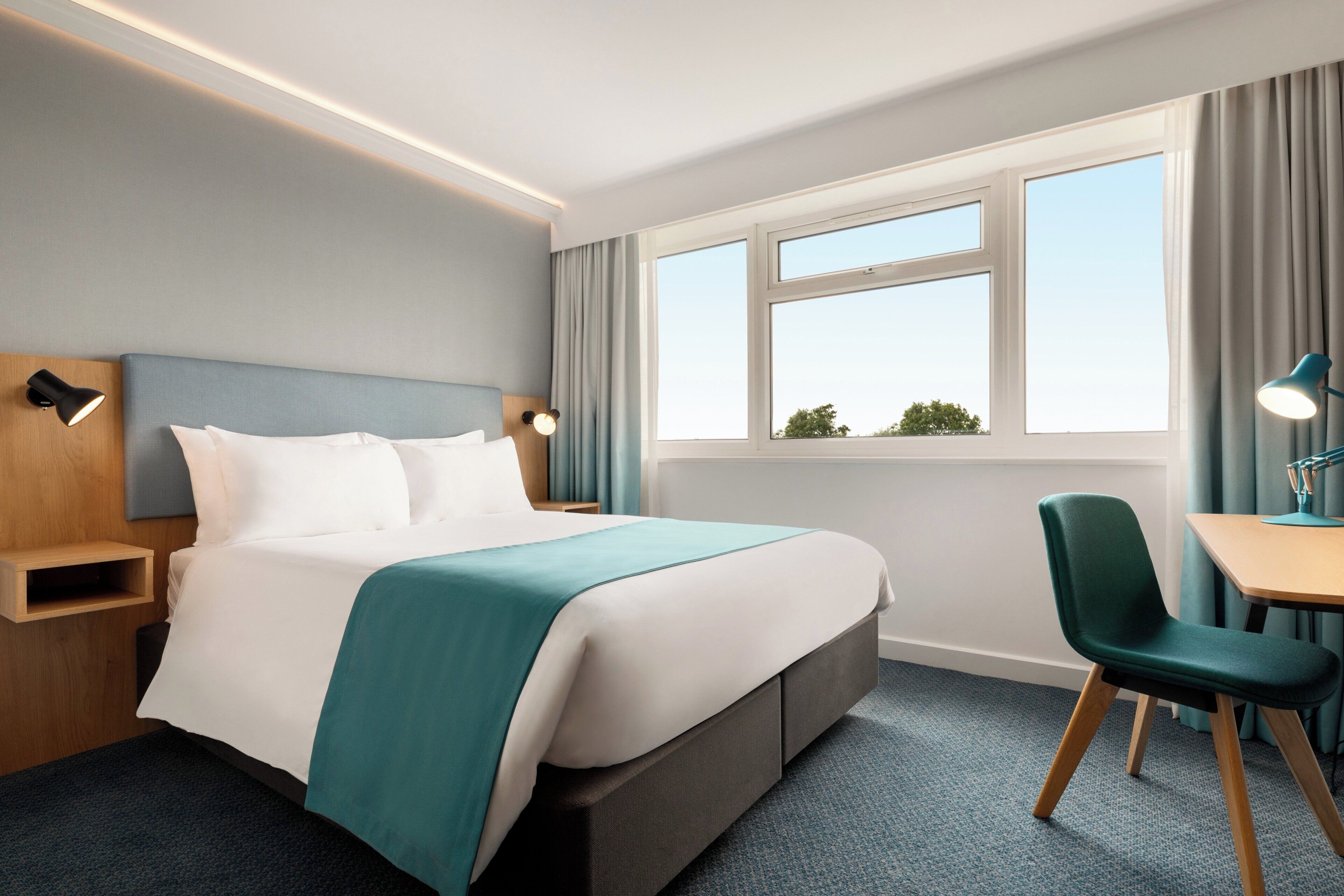 A hotel room with a bed, a desk, a chair, and a window with curtains.