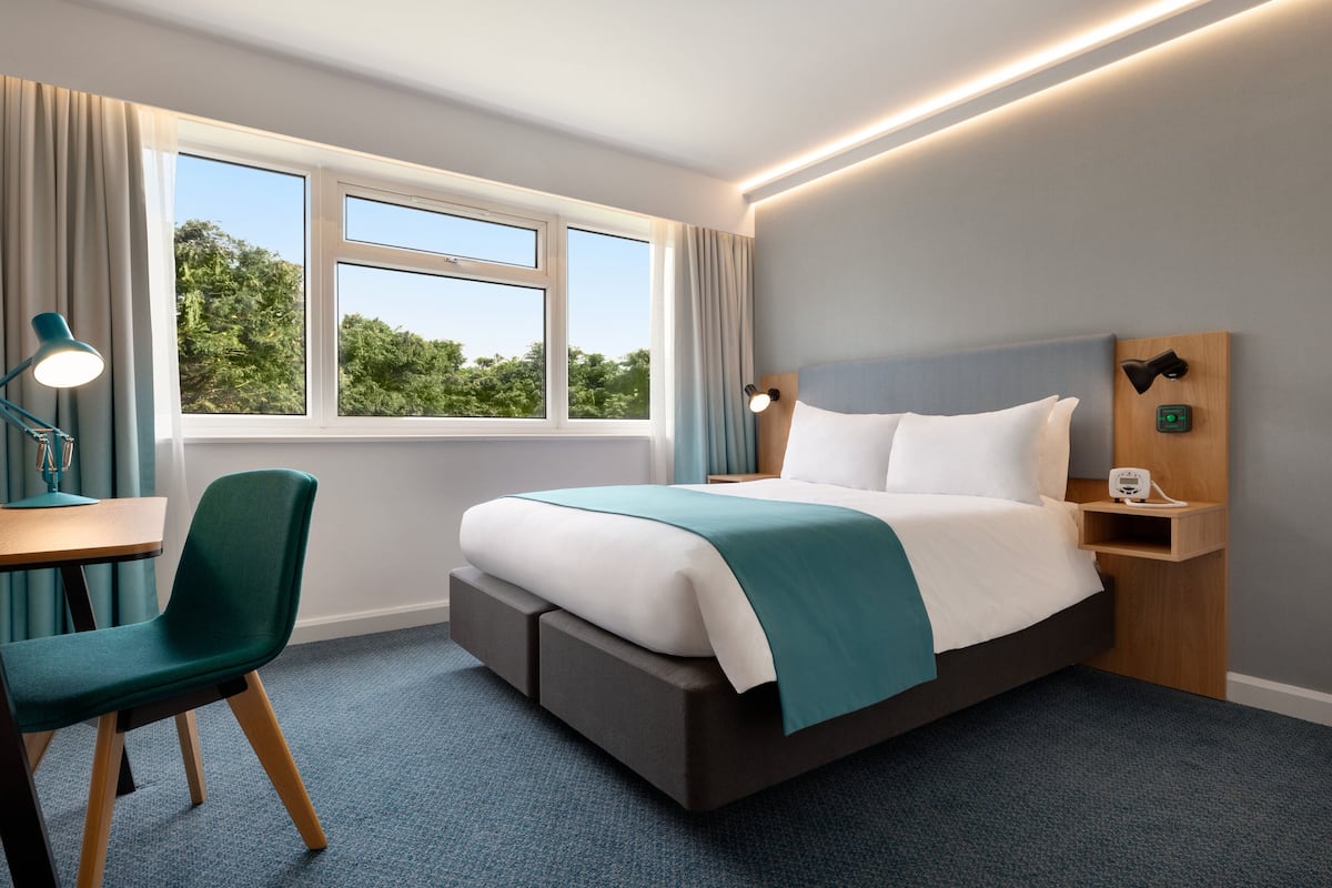 A modern hotel room with a large bed, a desk, and a chair.