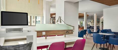 A modern interior with a white reception desk, a flat-screen monitor, a wooden accent wall, and vibrant seating areas.