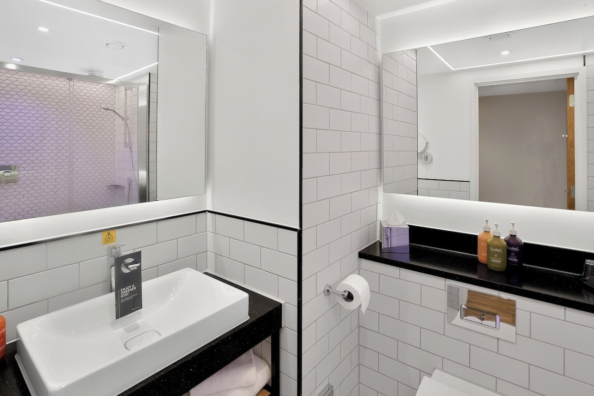 Un baño moderno con un lavabo blanco, encimera negra y un espejo.