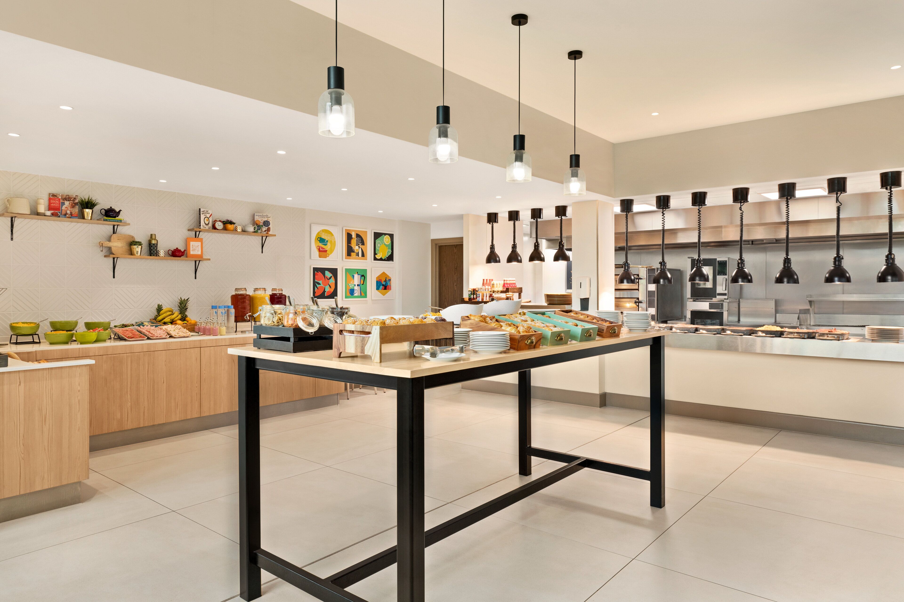 A modern kitchen with a central island, pendant lighting, and various food items displayed on shelves and the island.