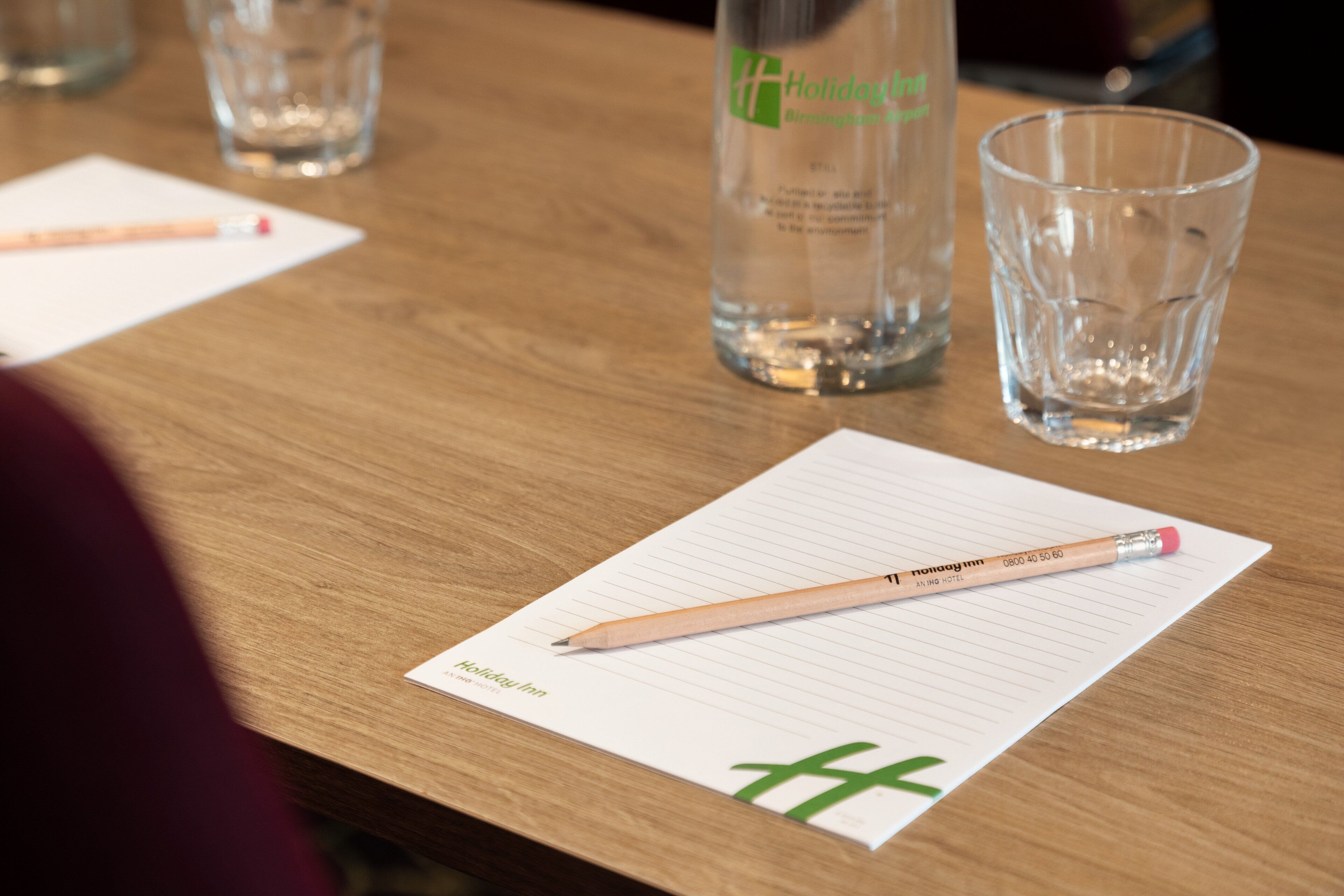 A wooden table with a lined notepad, a pencil, a glass of water, and a bottle of water.