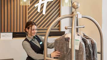 A person examining a coat on a display rack in a store with a wooden slat wall and a sign reading "IHG ONE REWARDS".
