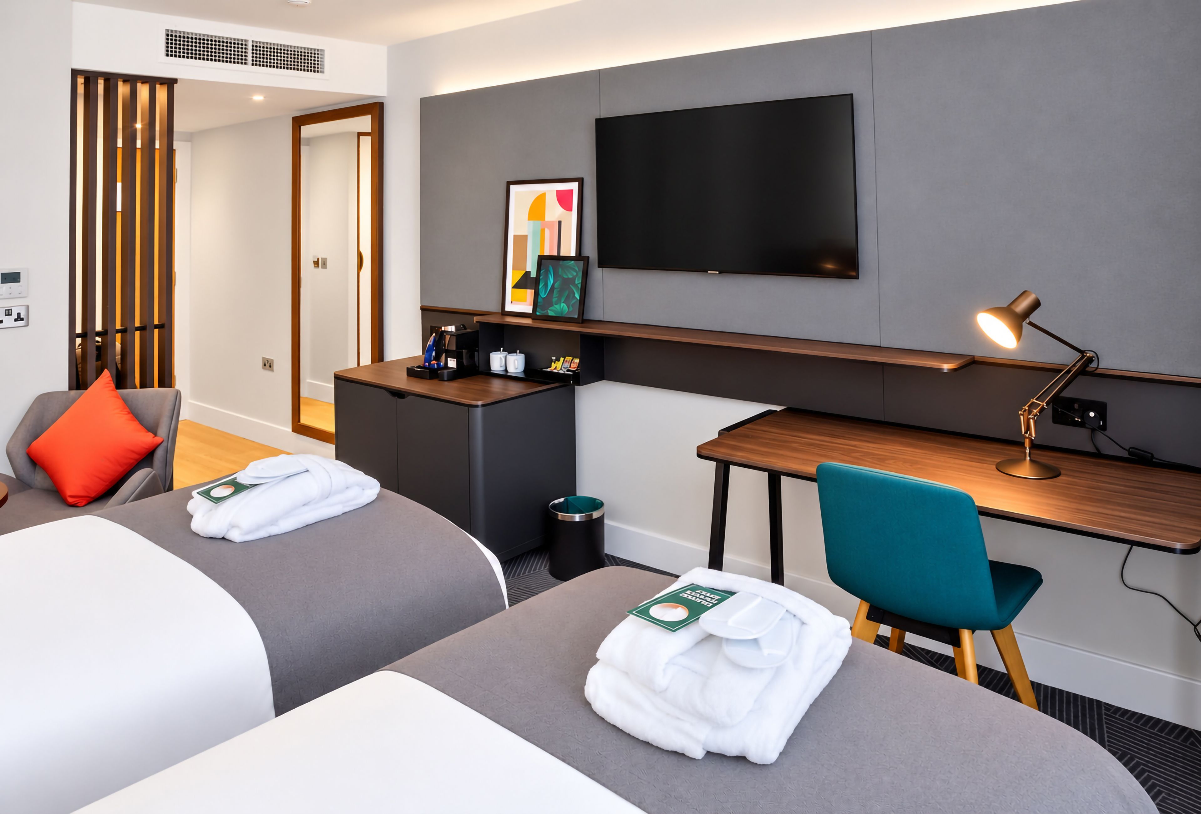 Habitación de hotel con dos camas, un escritorio, una silla, un televisor y una lámpara de escritorio.