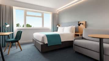 A hotel room with a bed, a desk, a chair, a sofa, and a window with curtains.
