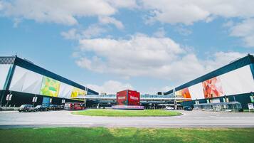A large exhibition center with a prominent red 'Welcome' sign, covered walkways, and a clear sky.