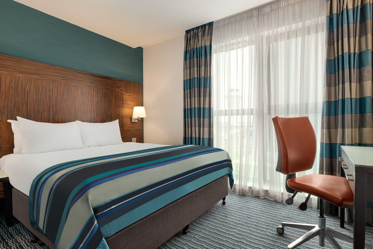 A hotel room with a large bed, a desk, and a chair.