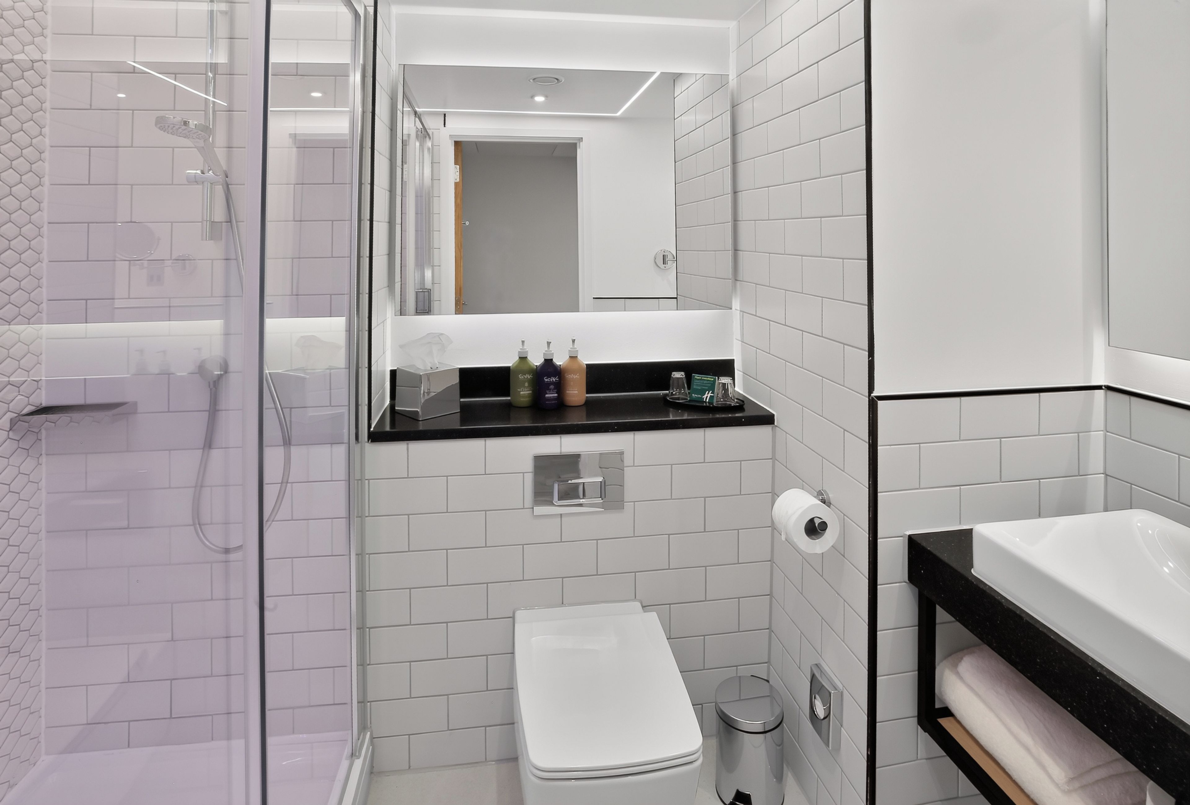 A modern bathroom with a glass shower enclosure, a white toilet, a black sink, and a mirror.
