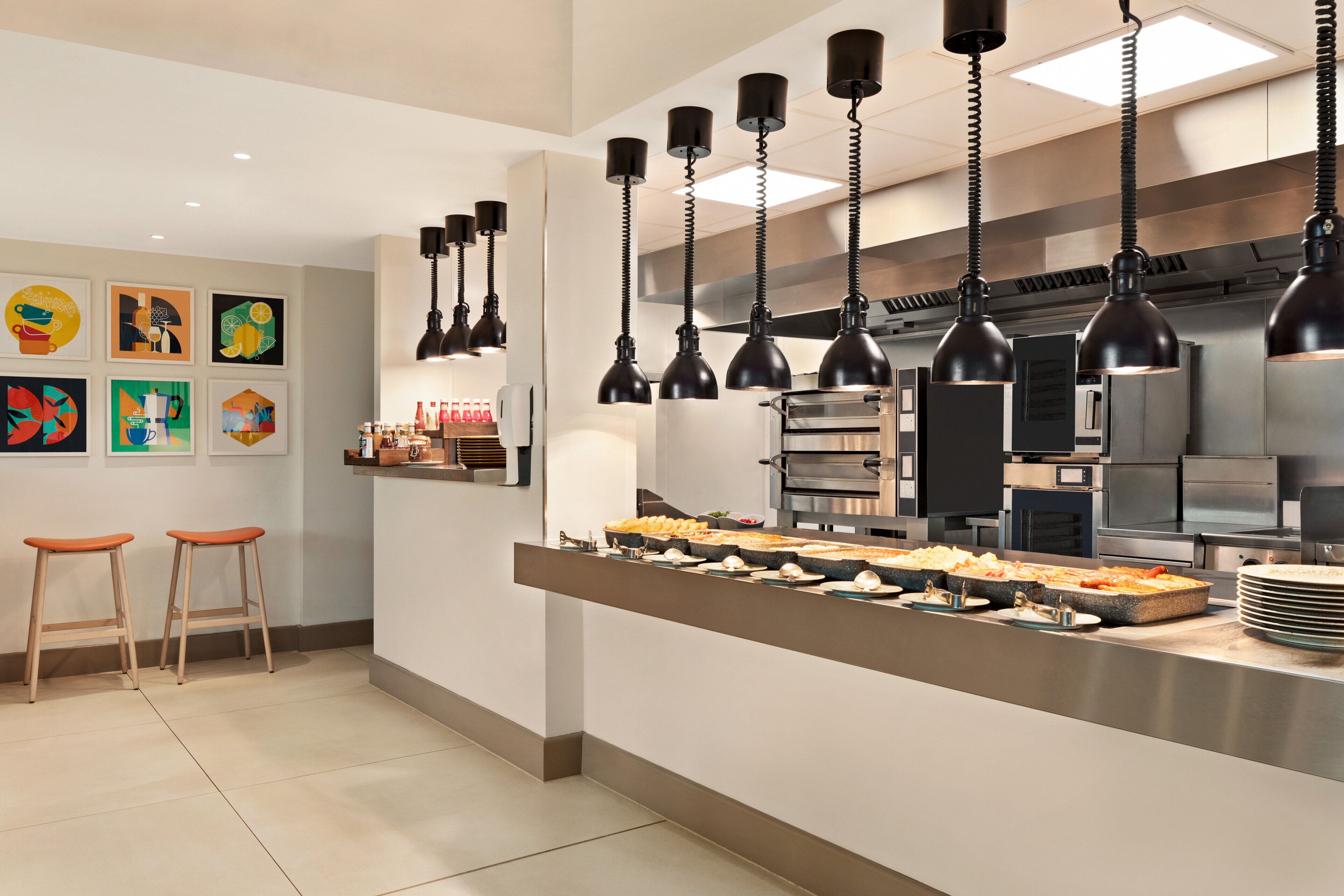 A modern kitchen with stainless steel appliances, black pendant lights, and a buffet counter with various dishes.