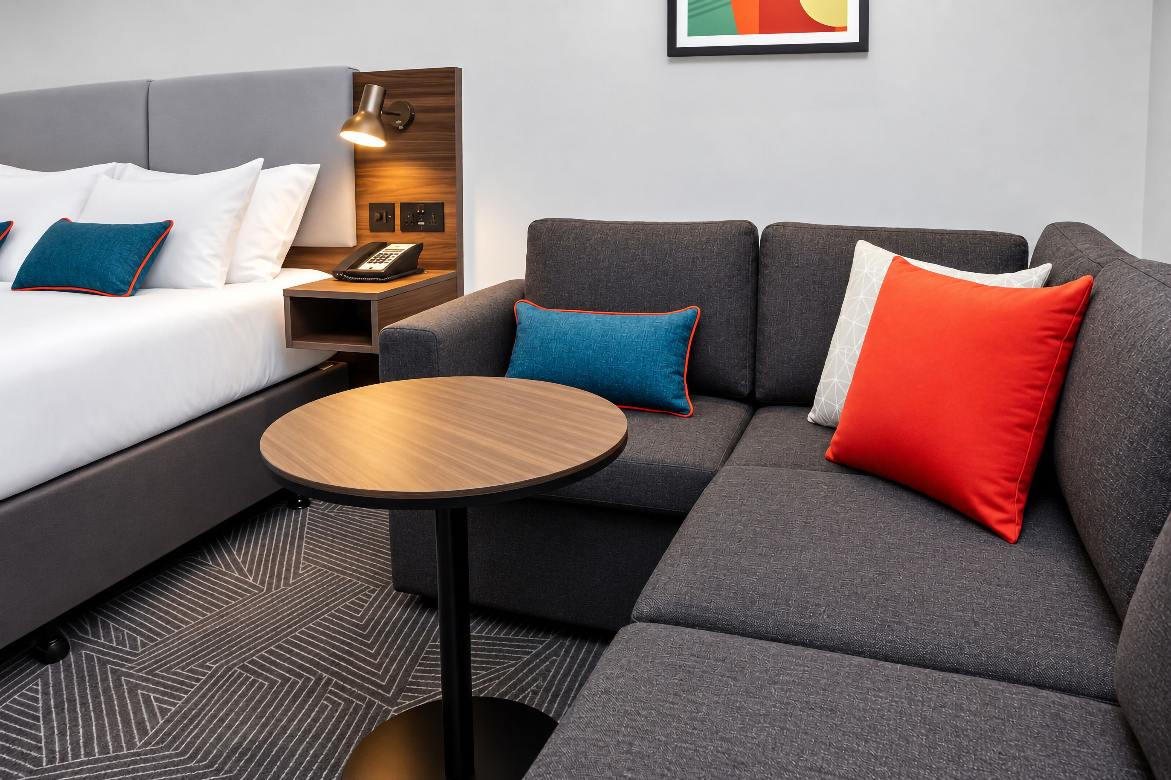 Una habitación de hotel moderna con cama, sofá, una mesita y una lámpara.