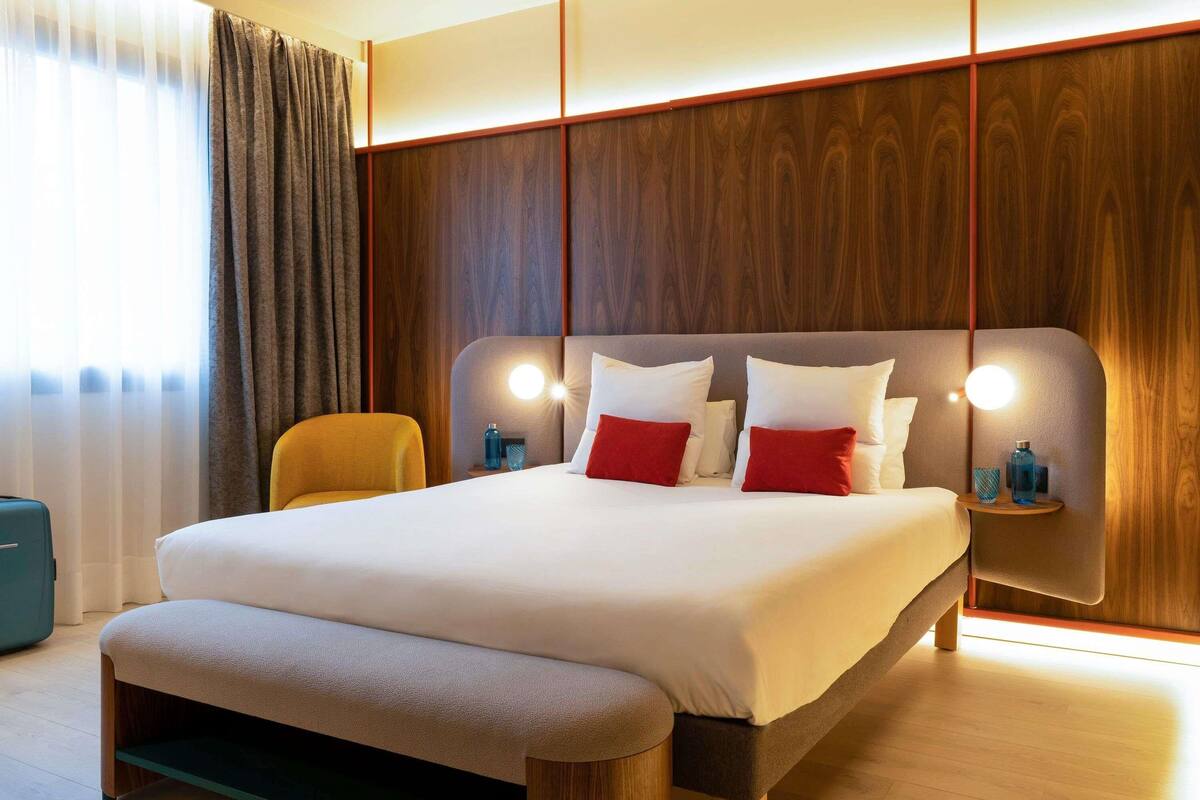 A modern hotel room with a large bed, a bench, wooden paneling, and bedside lamps.