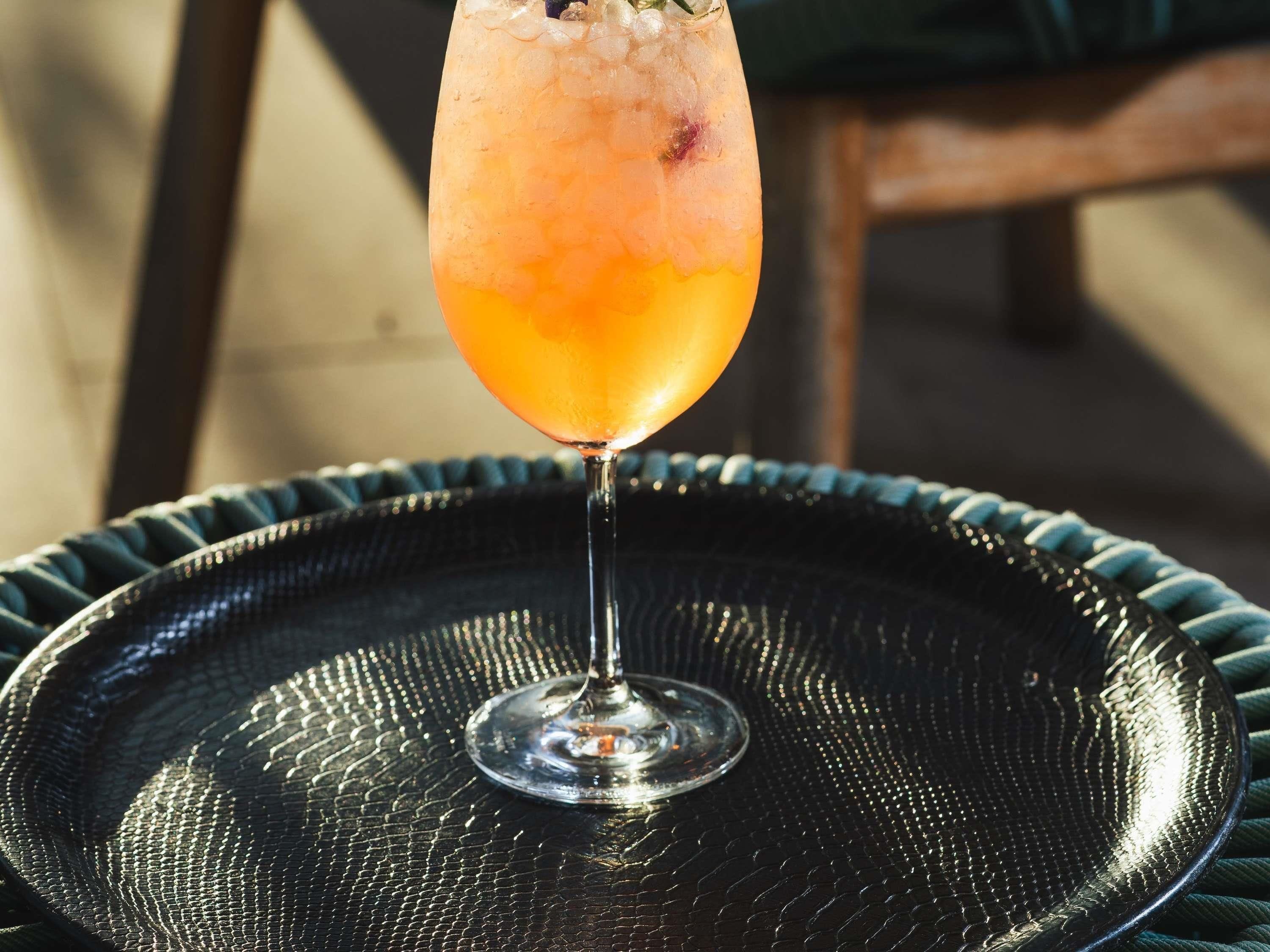 A glass of orange-colored drink on a textured black tray.