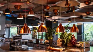 Una cocina moderna con lámparas colgantes de cobre, una isla de acero inoxidable y diversos utensilios de cocina.