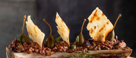 A dish with a bone, meat, and flatbread on a wooden board.