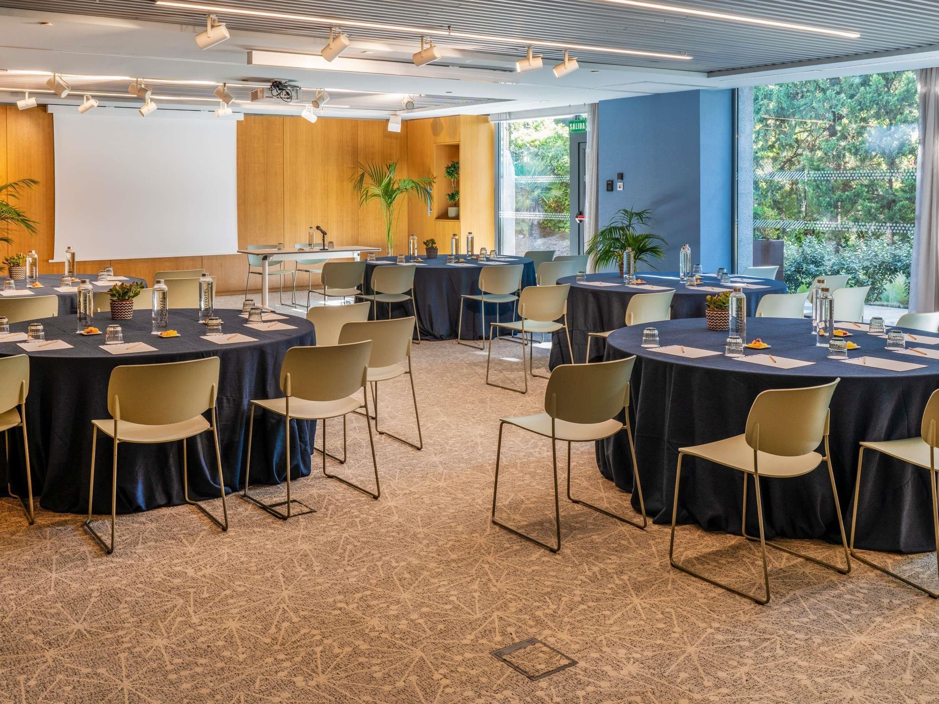 Une salle de conférence équipée de plusieurs tables rondes, de chaises et d’un écran de projection.