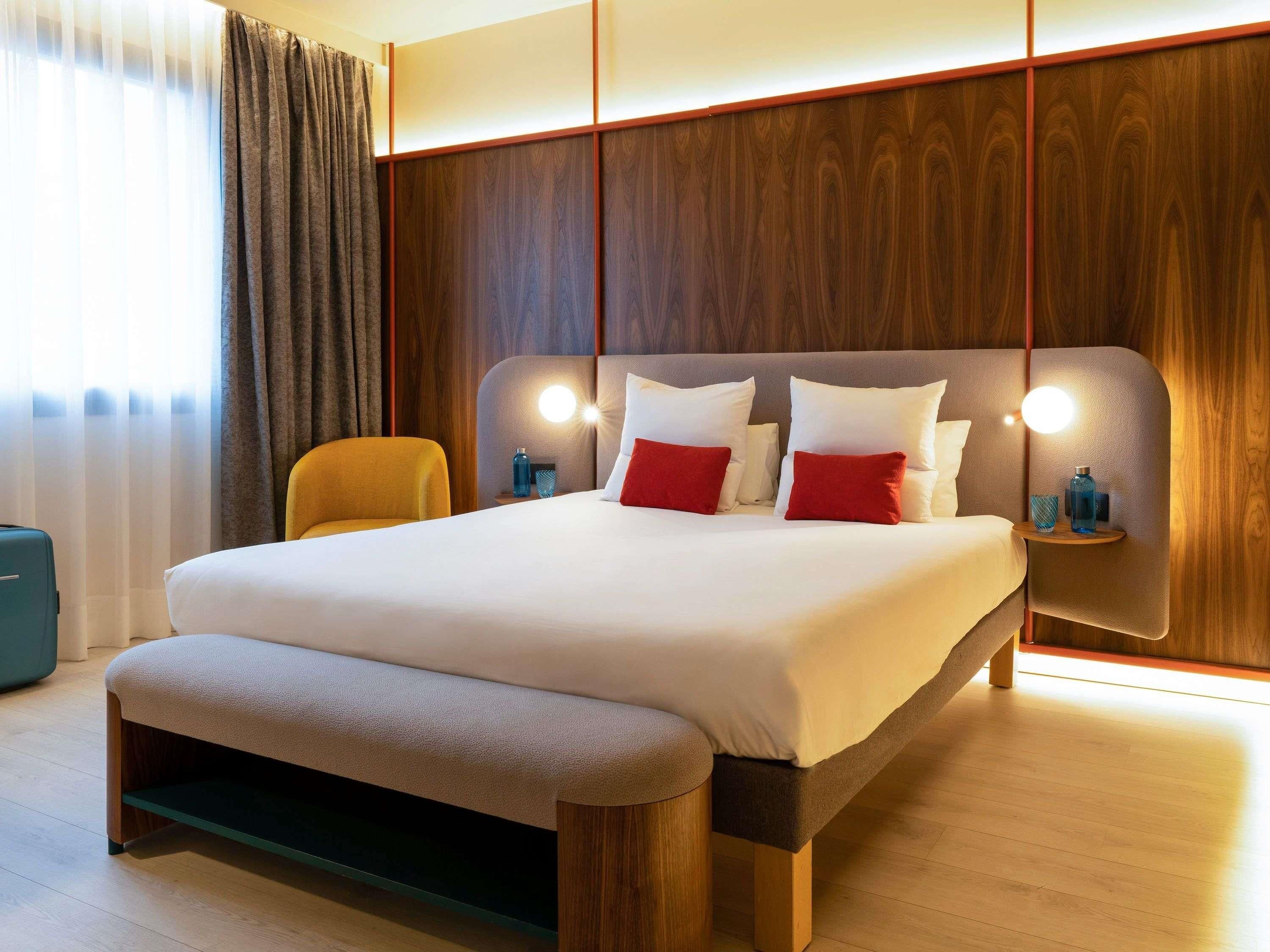 A modern hotel room with a large bed, a bench, wooden paneling, and bedside lamps.