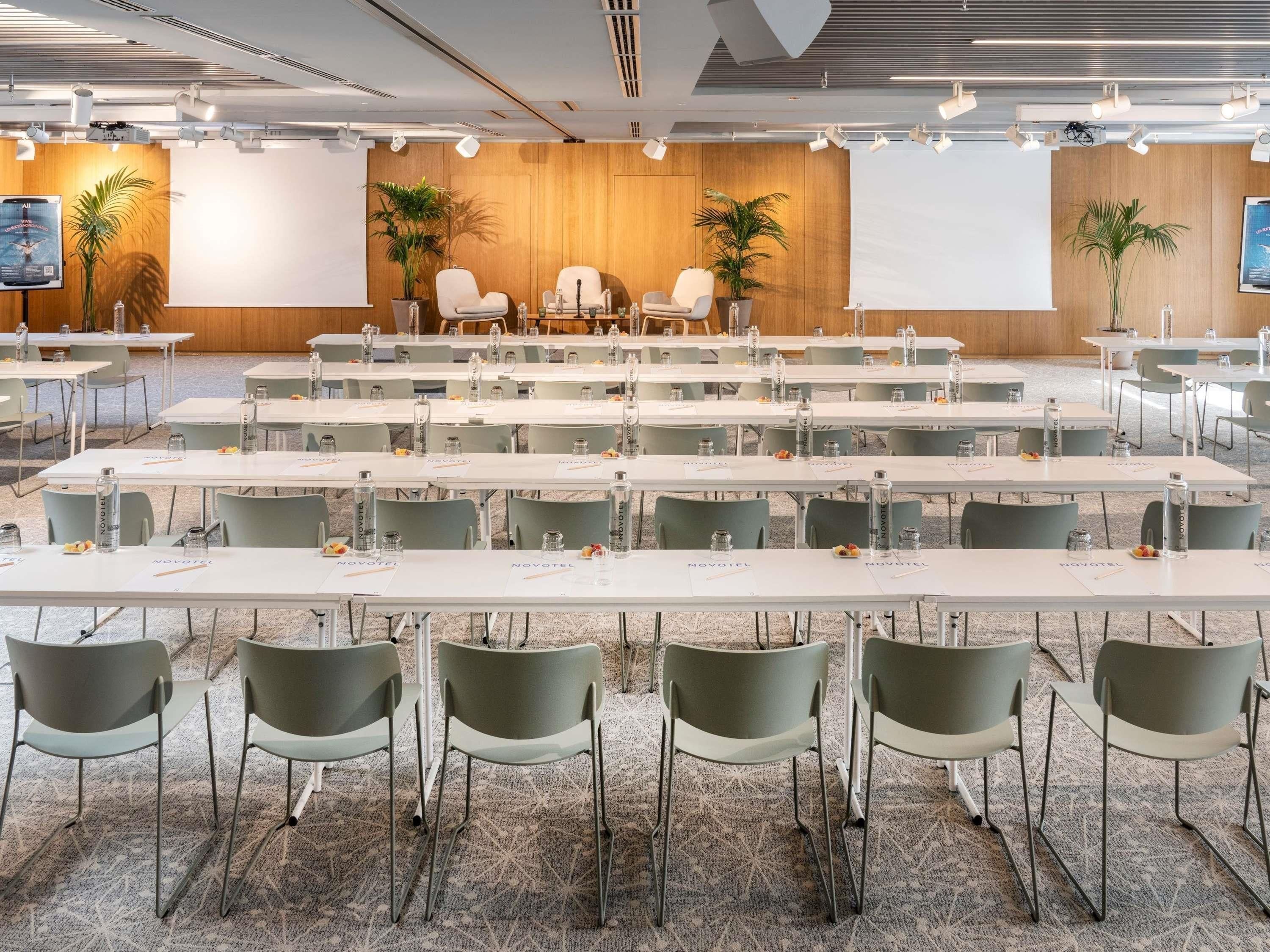 A conference room with multiple tables and chairs, a stage with a podium, and a large screen.