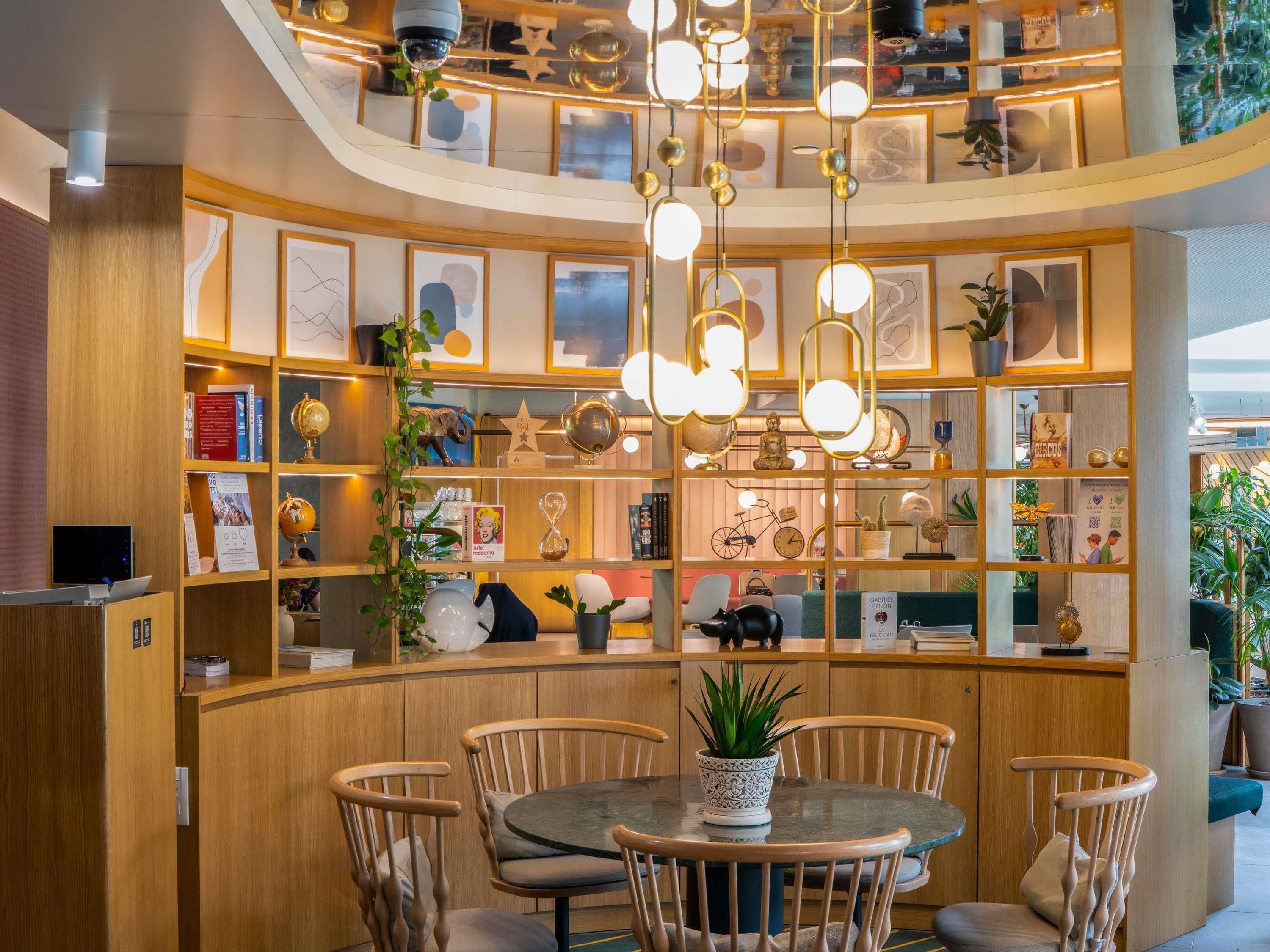 Un interior moderno con un mostrador de recepción de madera curvo, una mesa redonda con sillas y un techo con lámparas esféricas colgantes.