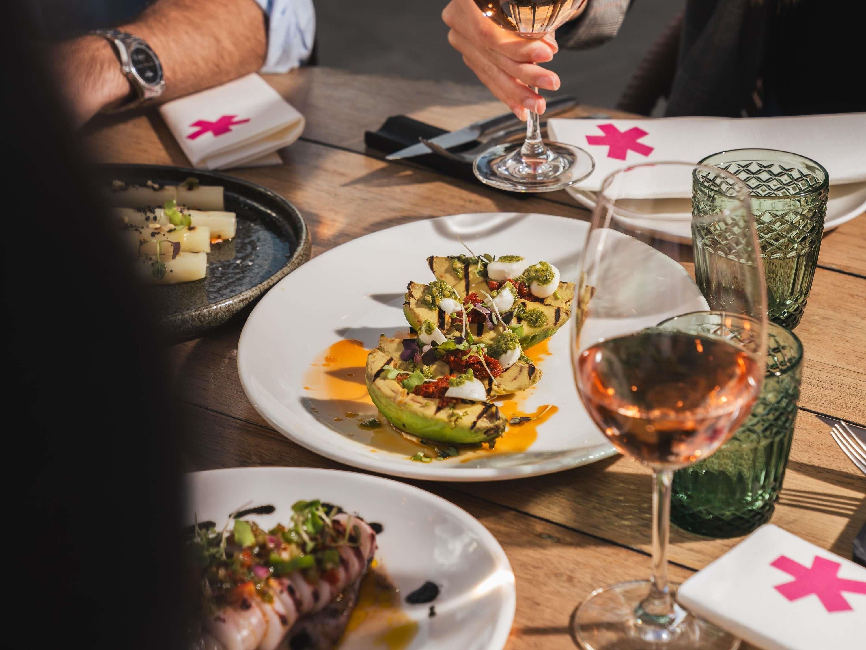 A dining table with plates of food, glasses of wine, and a watch on a wrist.