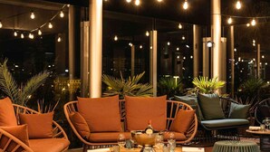 Un espacio al aire libre con sillas de mimbre, una mesa de madera y luces colgantes.