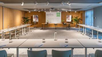 A modern conference room with long tables, chairs, and a banner advertising Novotel Madrid City Las Ventas.
