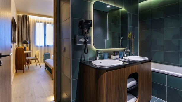 A modern bathroom with two sinks, a large mirror, and a hairdryer mounted on the wall.