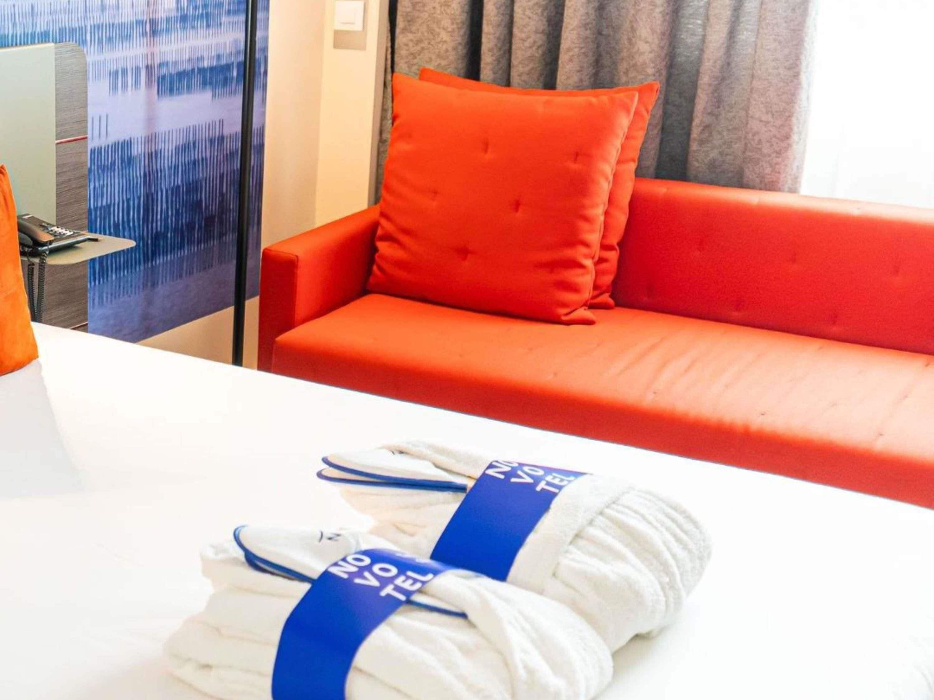 Une chambre d’hôtel avec un canapé rouge, une table blanche et une paire de serviettes blanches avec une étiquette bleue.