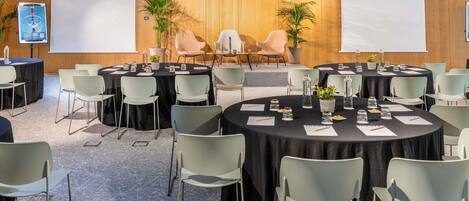 Un salón de conferencias con mesas redondas, sillas y un escenario con una pantalla.