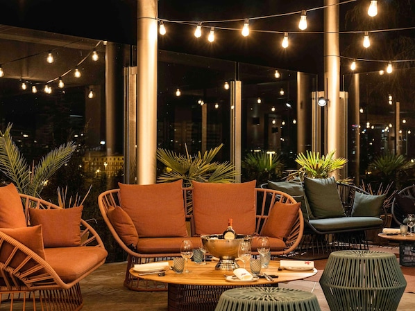 Un espacio al aire libre con sillas de mimbre, una mesa de madera y luces colgantes.