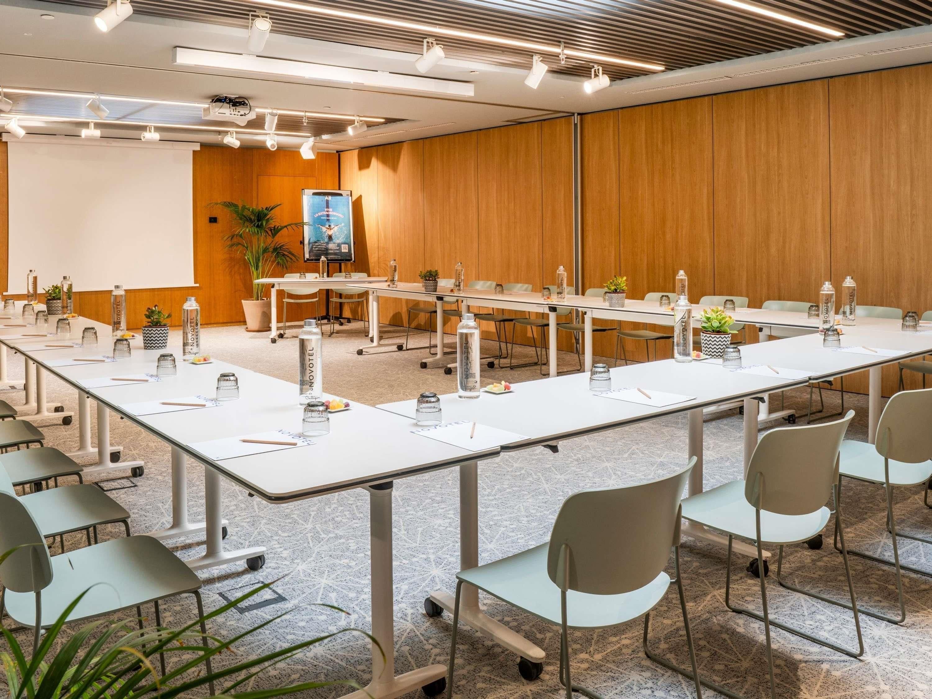 Un salón de conferencias con una larga mesa, sillas y una pantalla para proyector.