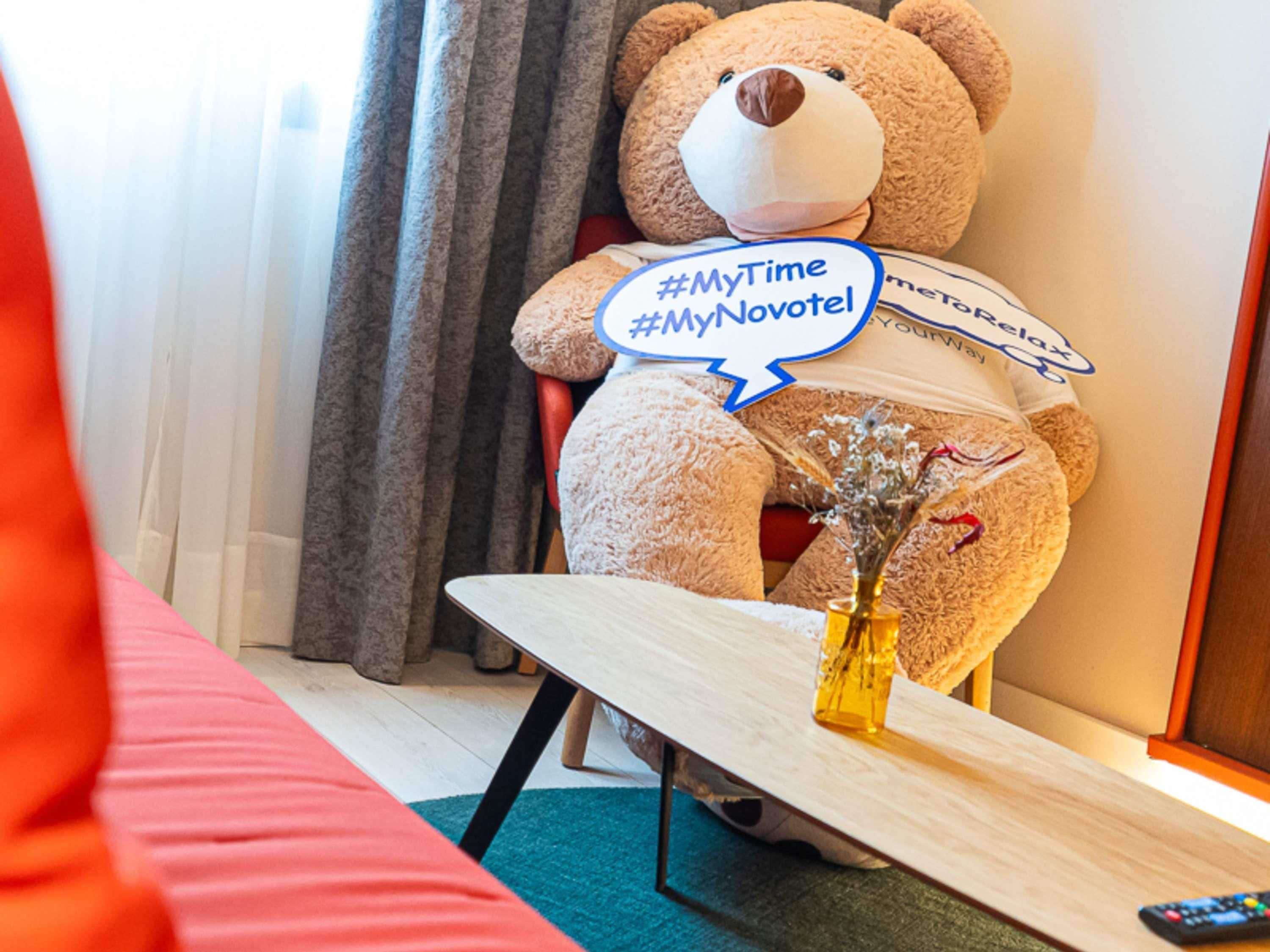 Un gran oso de peluche en una habitación de hotel con un bocadillo que dice '#MyTime #MyNovotel'.