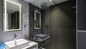 A modern bathroom with a large mirror, two sinks, a shower, and a glass-enclosed shower area.