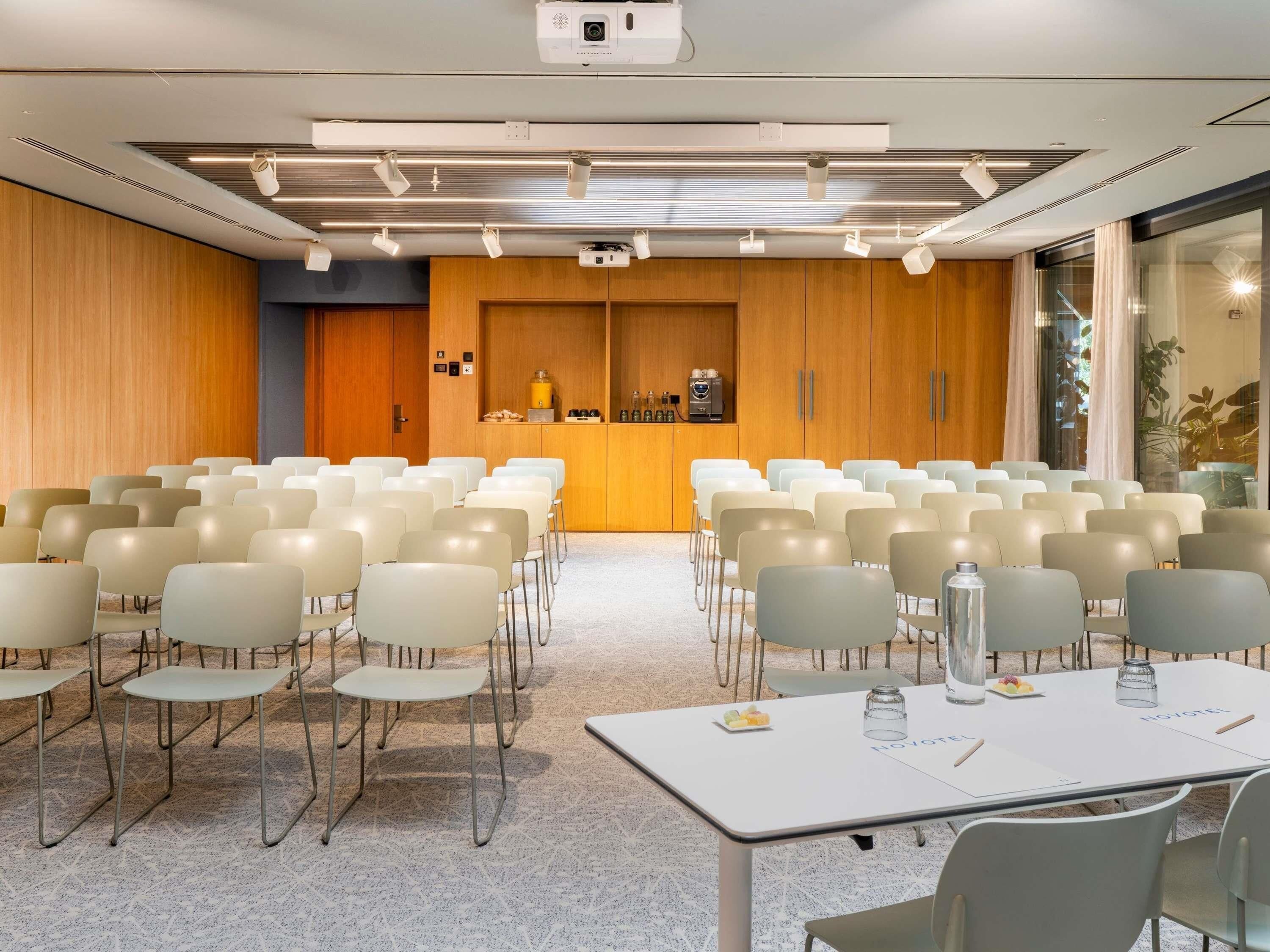 A conference room with rows of chairs, a projector, and a table with a nameplate.