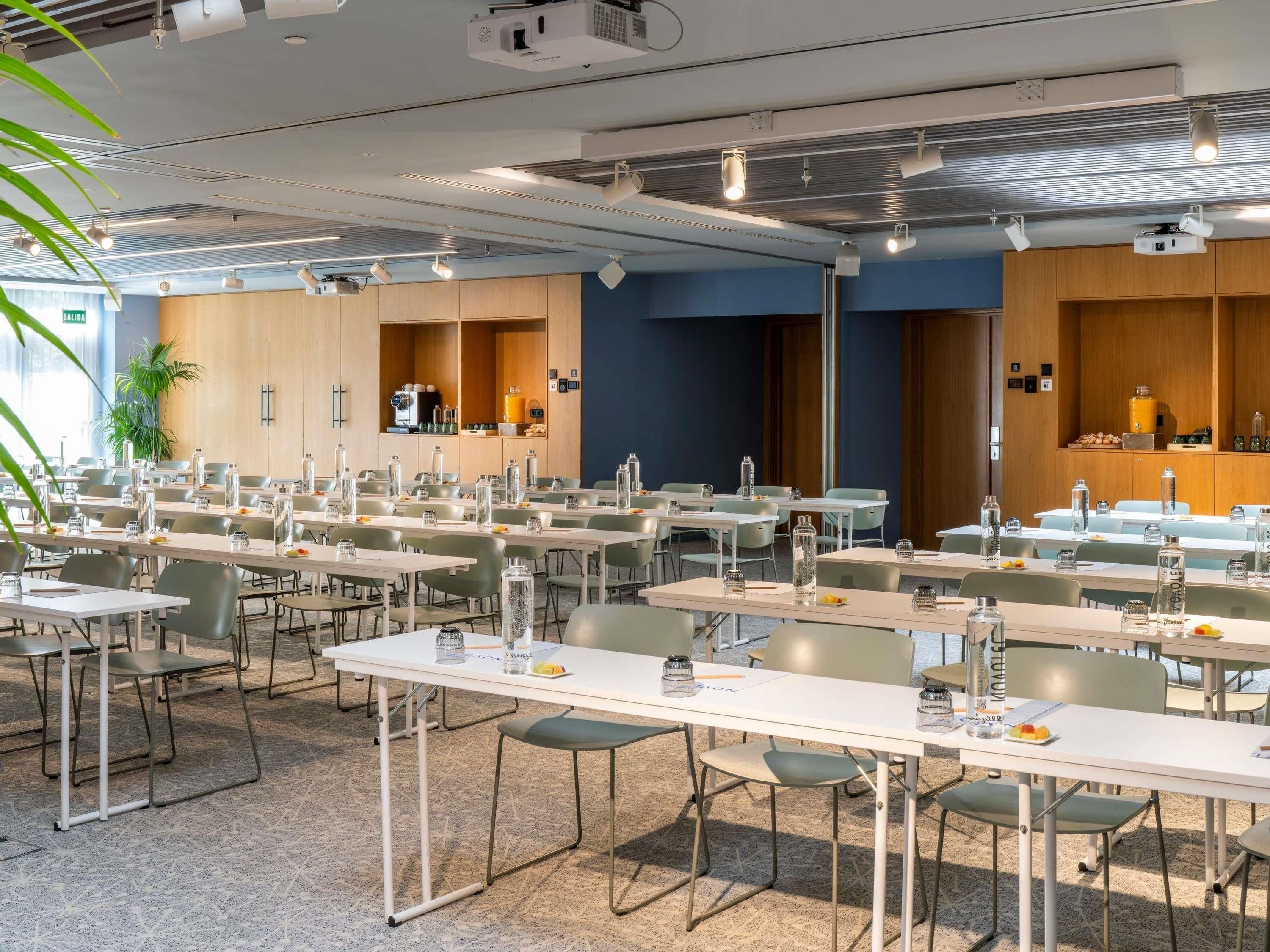 Een vergaderzaal met meerdere tafels, stoelen en een projectiescherm.