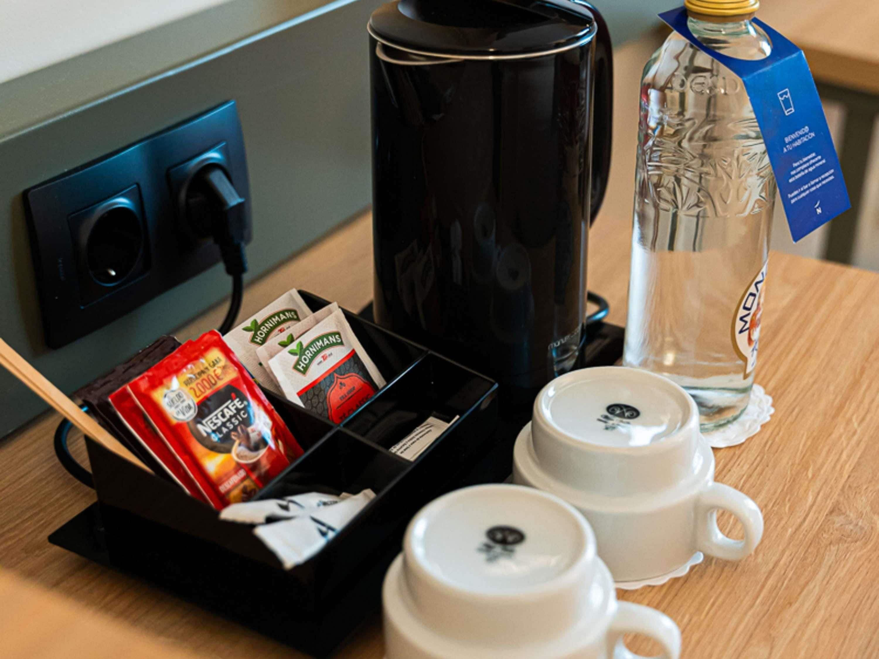Une machine à café, deux tasses, une bouteille d’eau et une boîte de capsules de café sur une table en bois.