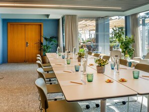 Un salón de conferencias con una larga mesa, sillas y plantas en macetas.