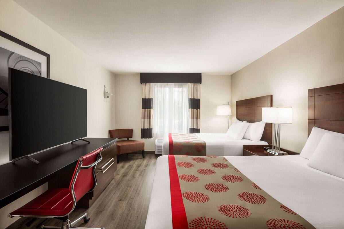 Une chambre d’hôtel avec un lit, un bureau, une chaise, une télévision et une fenêtre avec des rideaux.
