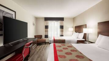 Habitación de hotel con cama, escritorio, silla, televisión y ventana con cortinas.