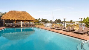 Una piscina con sillas de descanso y una estructura de techo de paja.