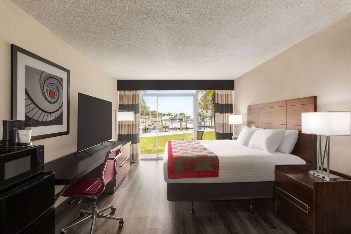 Une chambre d’hôtel équipée d’un lit, d’un bureau, d’une chaise et d’une grande fenêtre donnant sur l’extérieur.