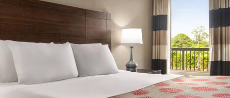 Habitación de hotel con una cama grande, una mesita de noche con lámpara y un balcón con cortinas.
