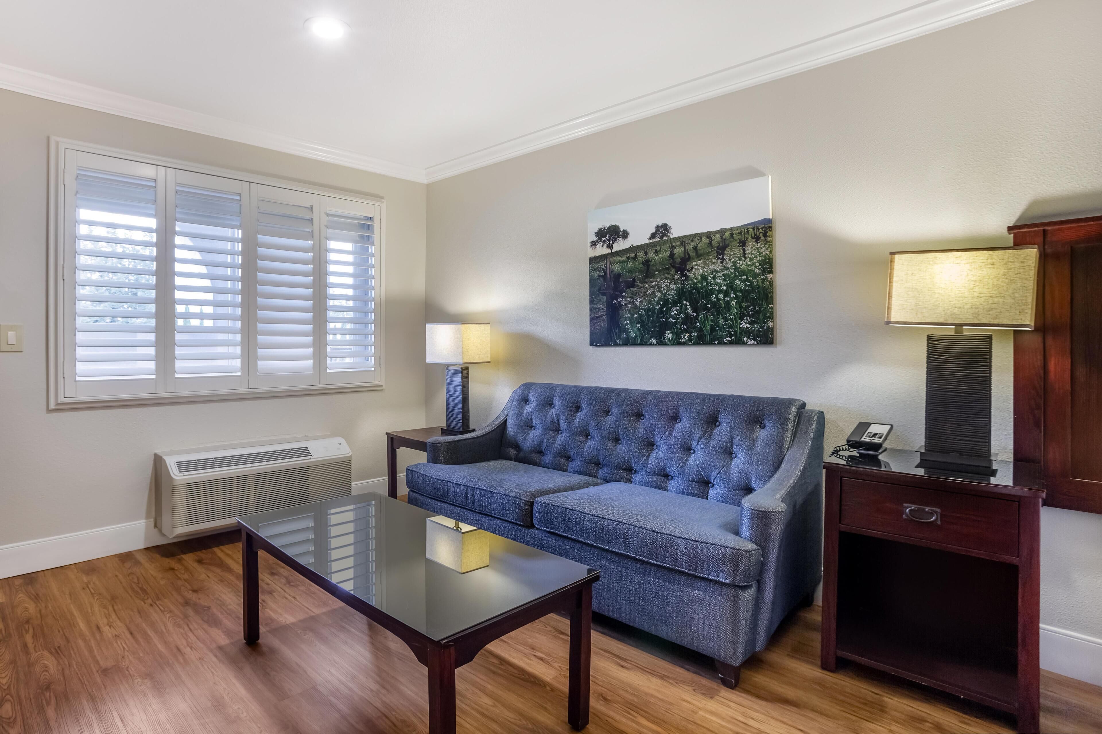 A living room with a blue sofa, a glass coffee table, a lamp, and a painting on the wall.