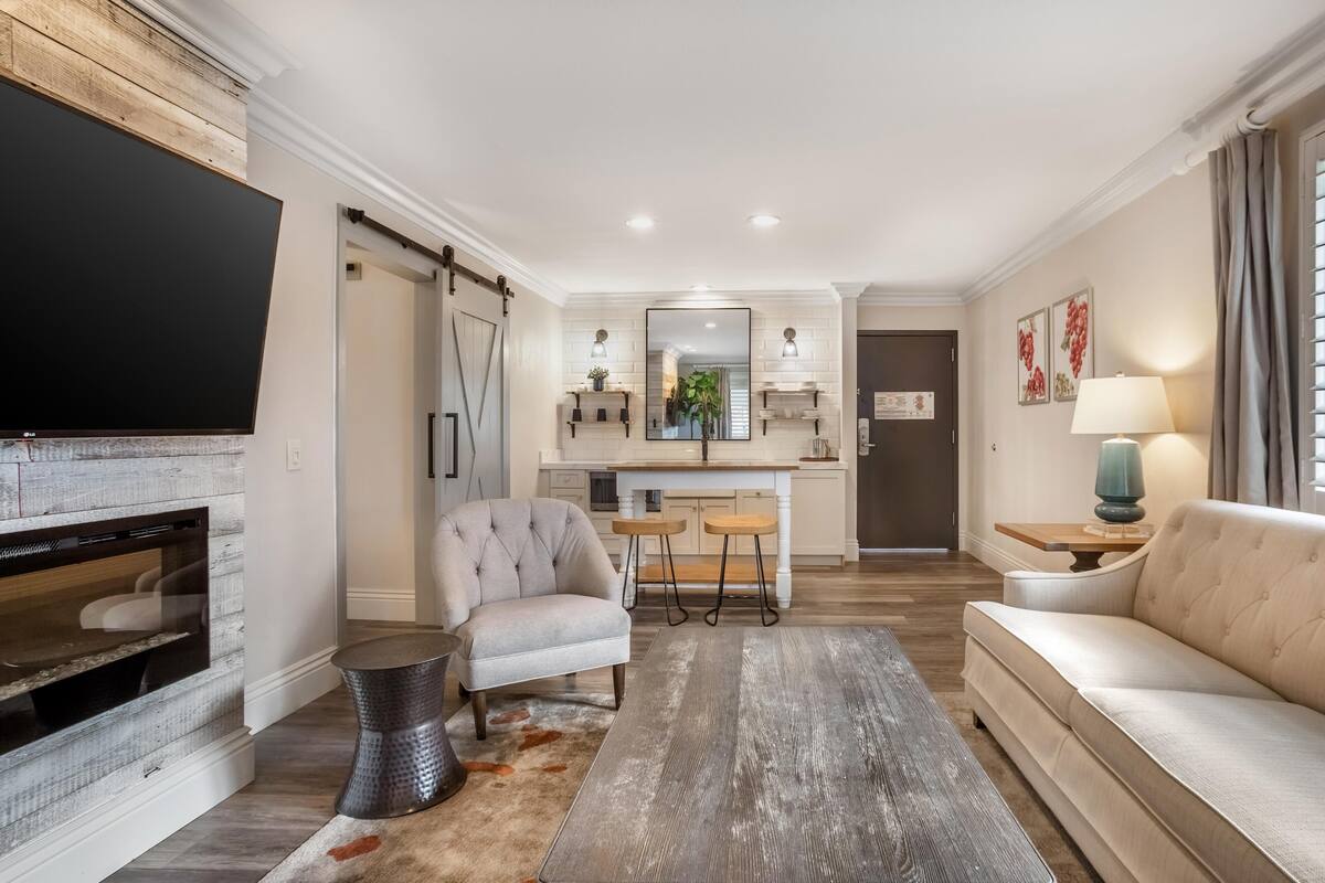 A living room with a fireplace, sofa, and coffee table. There is a kitchen area with a dining table and chairs.