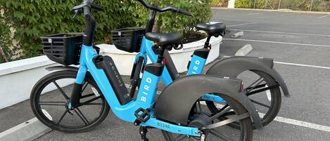 A blue electric bicycle with a basket and a rear rack parked in a parking lot.