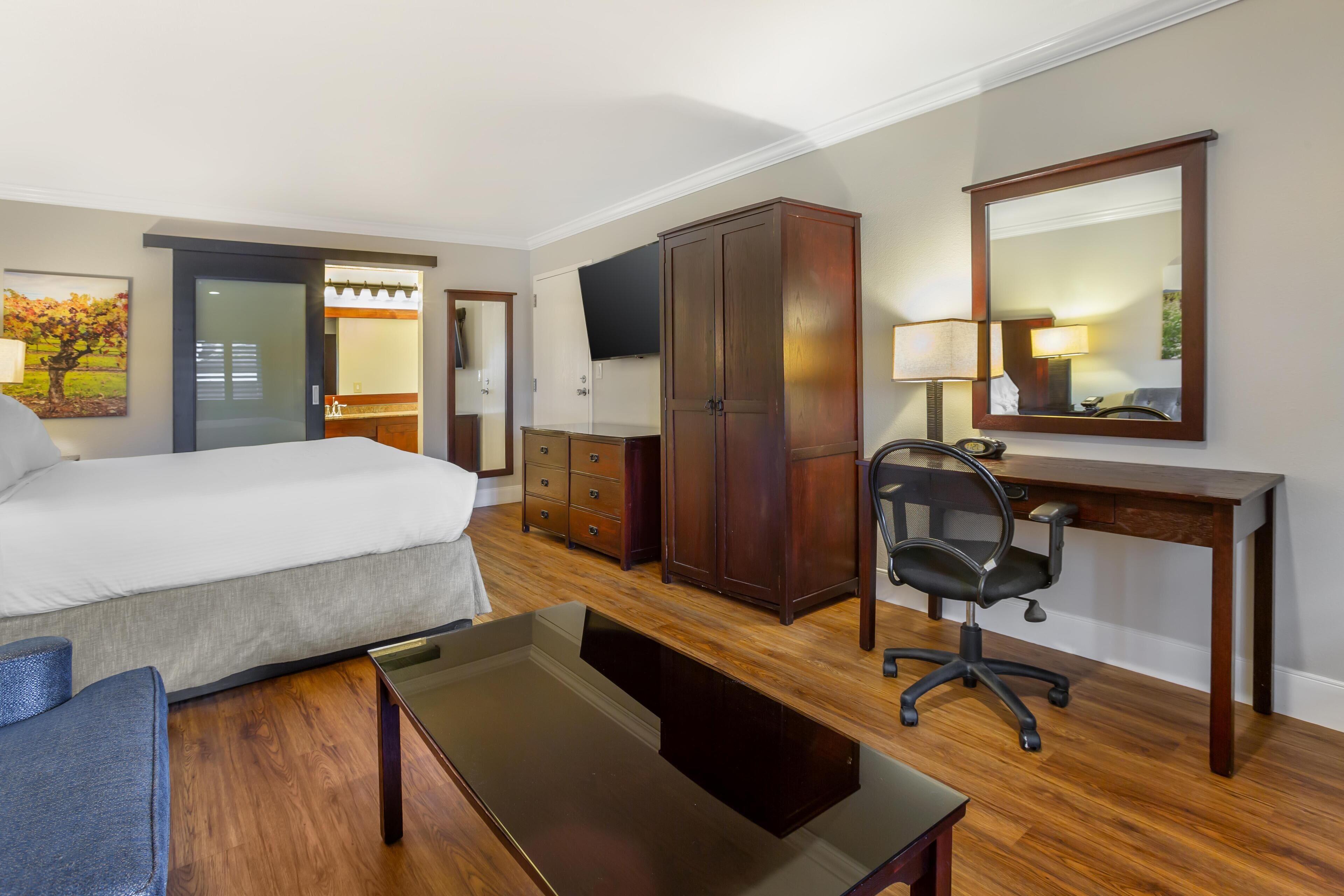 A hotel room with a bed, a desk, a chair, a wardrobe, and a television.