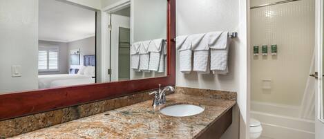 A bathroom with a granite countertop sink, a large mirror, a shower, and a toilet.