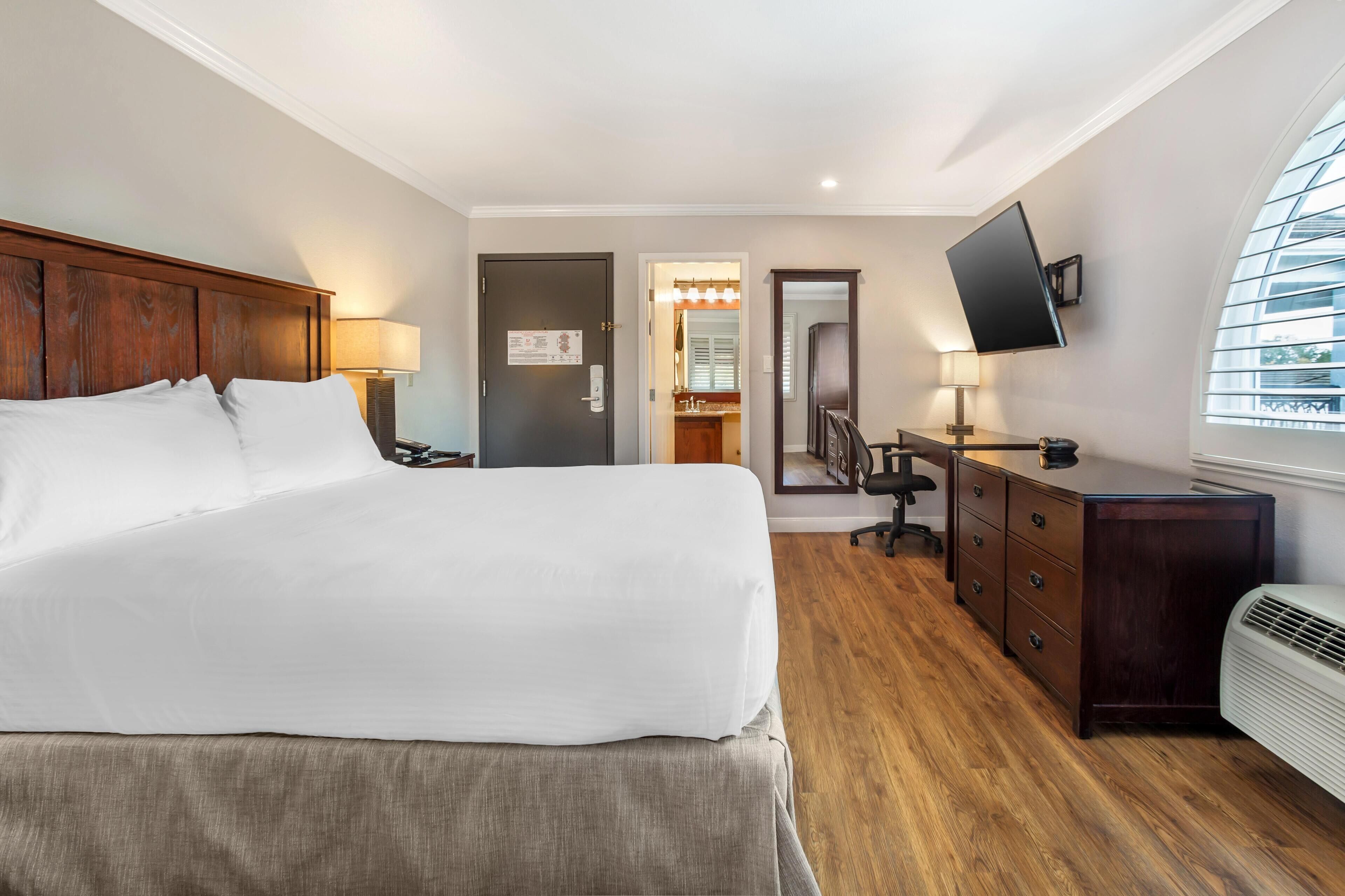 Een hotelkamer met een groot bed, een bureau met stoel, een aan de muur bevestigde televisie en een raam met zonwering.