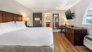 Een hotelkamer met een groot bed, een bureau met stoel, een aan de muur bevestigde televisie en een raam met zonwering.