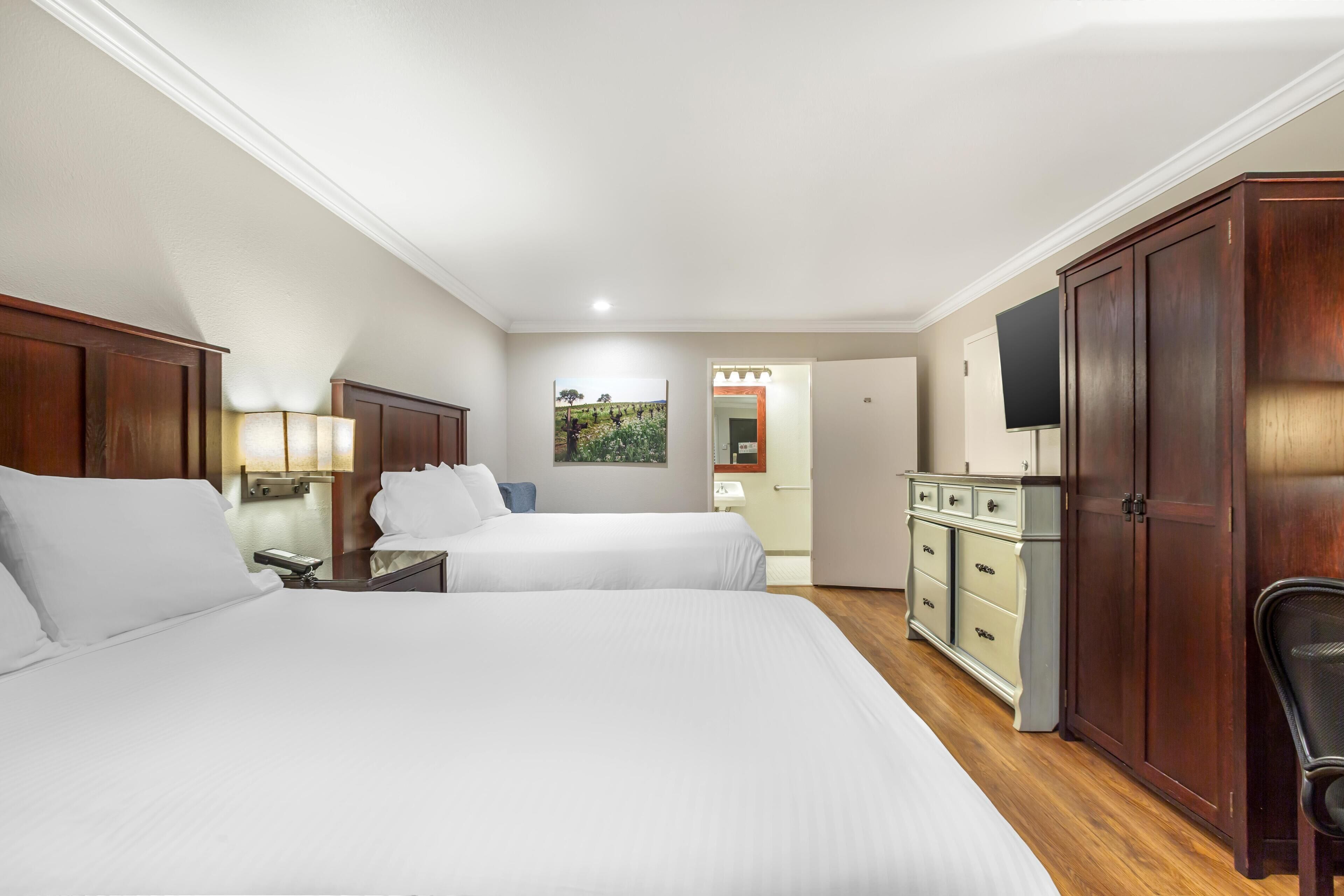 A hotel room with two beds, a dresser, a TV, and a painting on the wall.