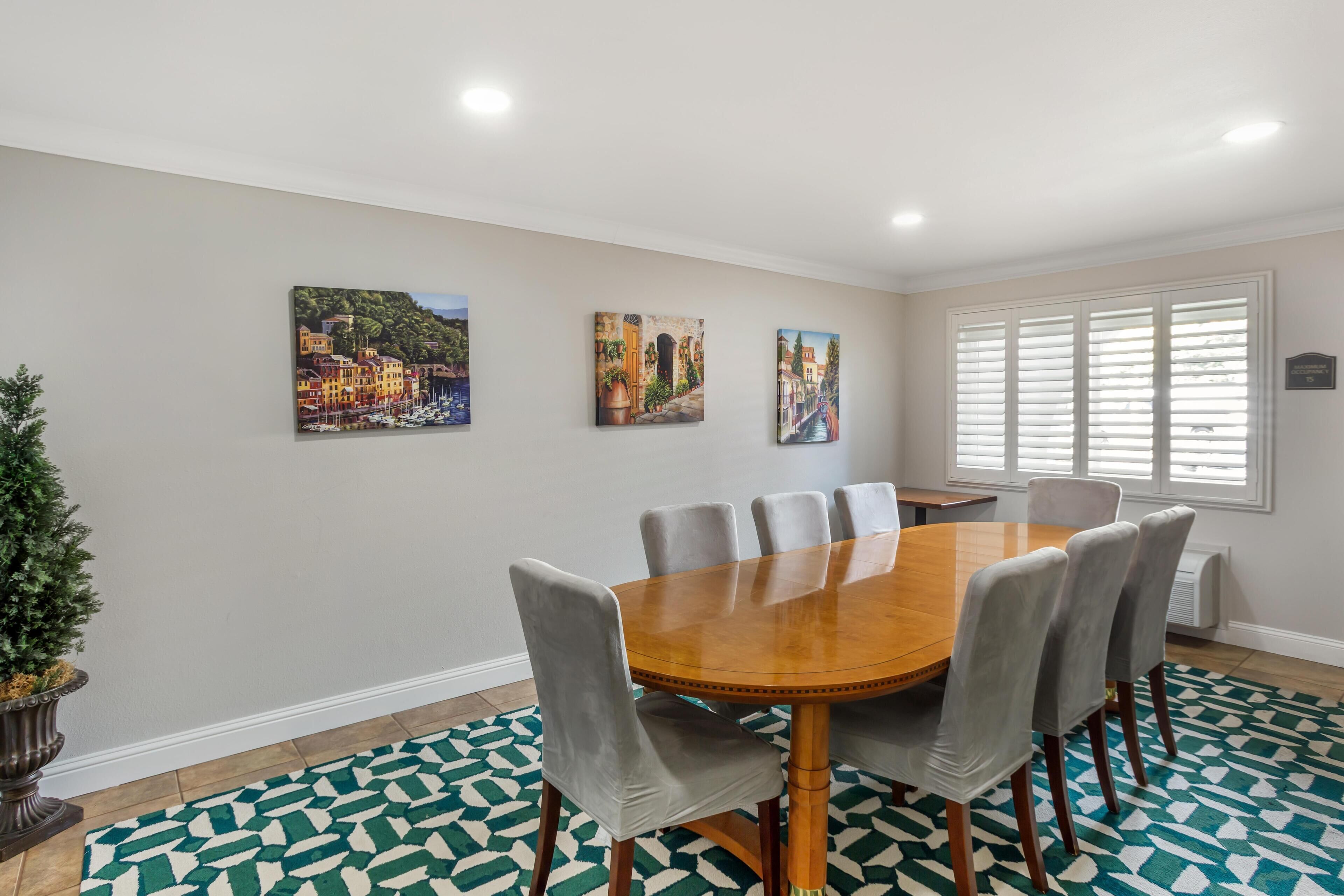 A conference room with a wooden table, six grey upholstered chairs, and three paintings on the wall.